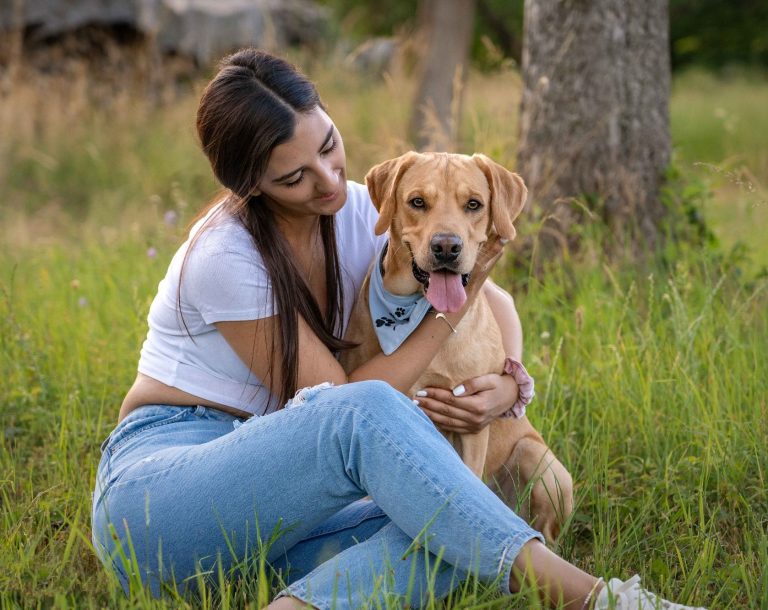 Ein Hund und sein Frauchen sitzen in einer Weise nebeneinander. Das Frauchen umarmt den Hund.